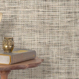 End table with a phone, book and owl sculpture in front of a wall covered in paperweave grasscloth in mottled cream and black.