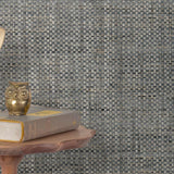 End table with a phone, book and owl sculpture in front of a wall covered in paperweave grasscloth in mottled blue-gray and tan.