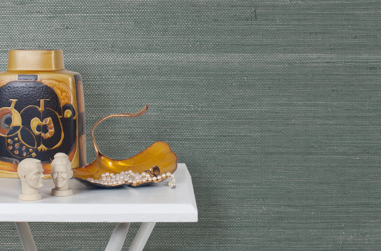 End table with a vase and sculptures in front of a wall papered in pearlized jute grasscloth in gray-blue.
