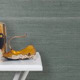 End table with a vase and sculptures in front of a wall papered in pearlized jute grasscloth in gray-blue.