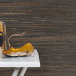 End table with a vase and sculptures in front of a wall papered in jute grasscloth in black and brown.