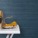 End table with a vase and sculptures in front of a wall papered in jute grasscloth in navy blue.