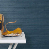 End table with a vase and sculptures in front of a wall papered in jute grasscloth in navy blue.