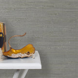 End table with a vase and sculptures in front of a wall papered in jute grasscloth in gray.