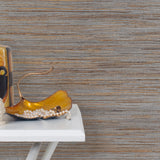End table with a vase and sculptures in front of a wall papered in metallic-rubbed jute grasscloth in gray and tan.