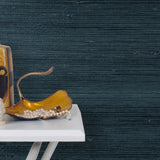 End table with a vase and sculptures in front of a wall papered in jute grasscloth in dark navy.