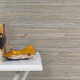 End table with a vase and sculptures in front of a wall papered in jute grasscloth in gray and tan.