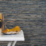 End table with a vase and sculptures in front of a wall papered in metallic-rubbed jute grasscloth in black and gray.