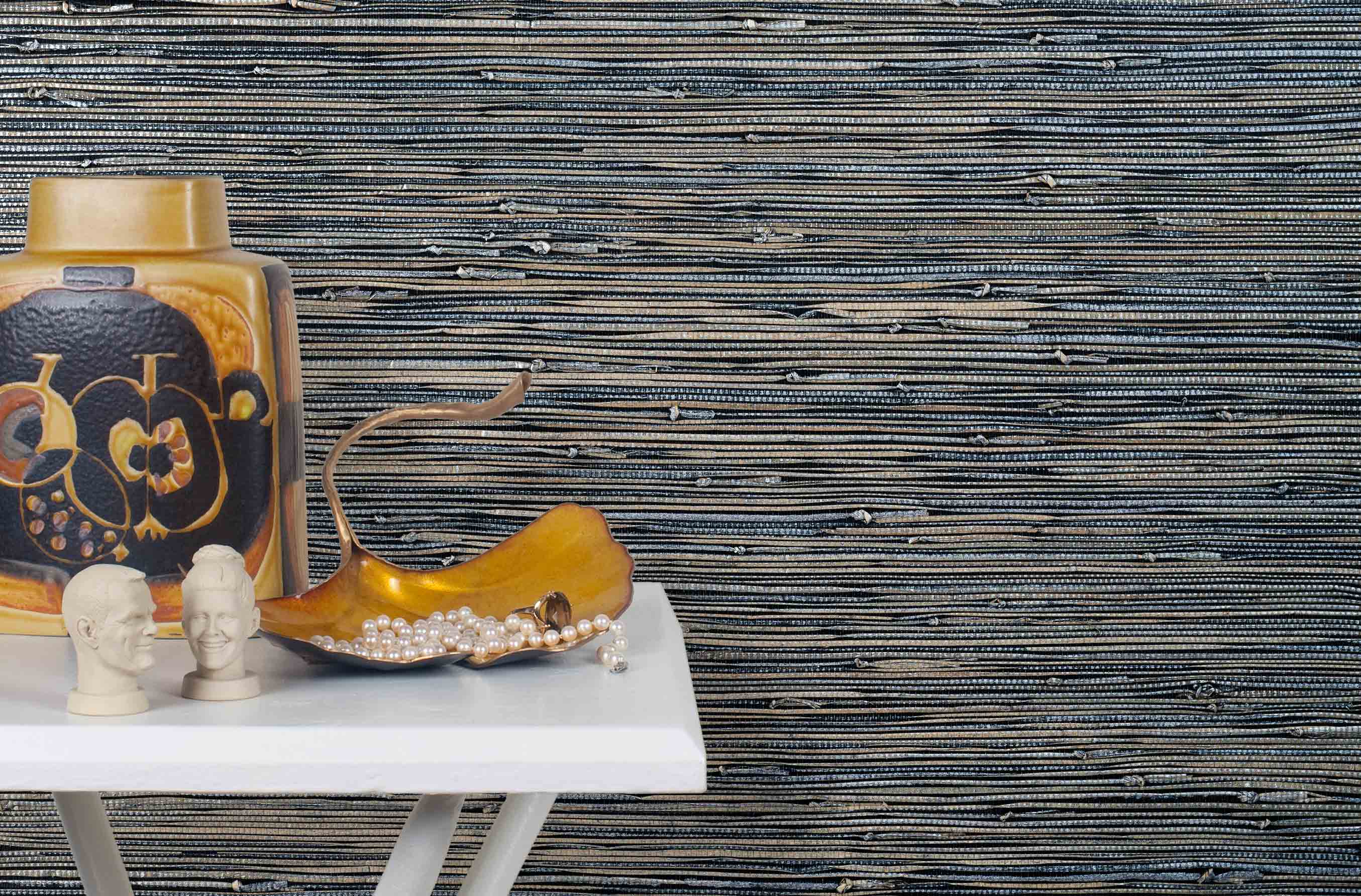 End table with a vase and sculptures in front of a wall papered in metallic-rubbed jute grasscloth in black and gray.