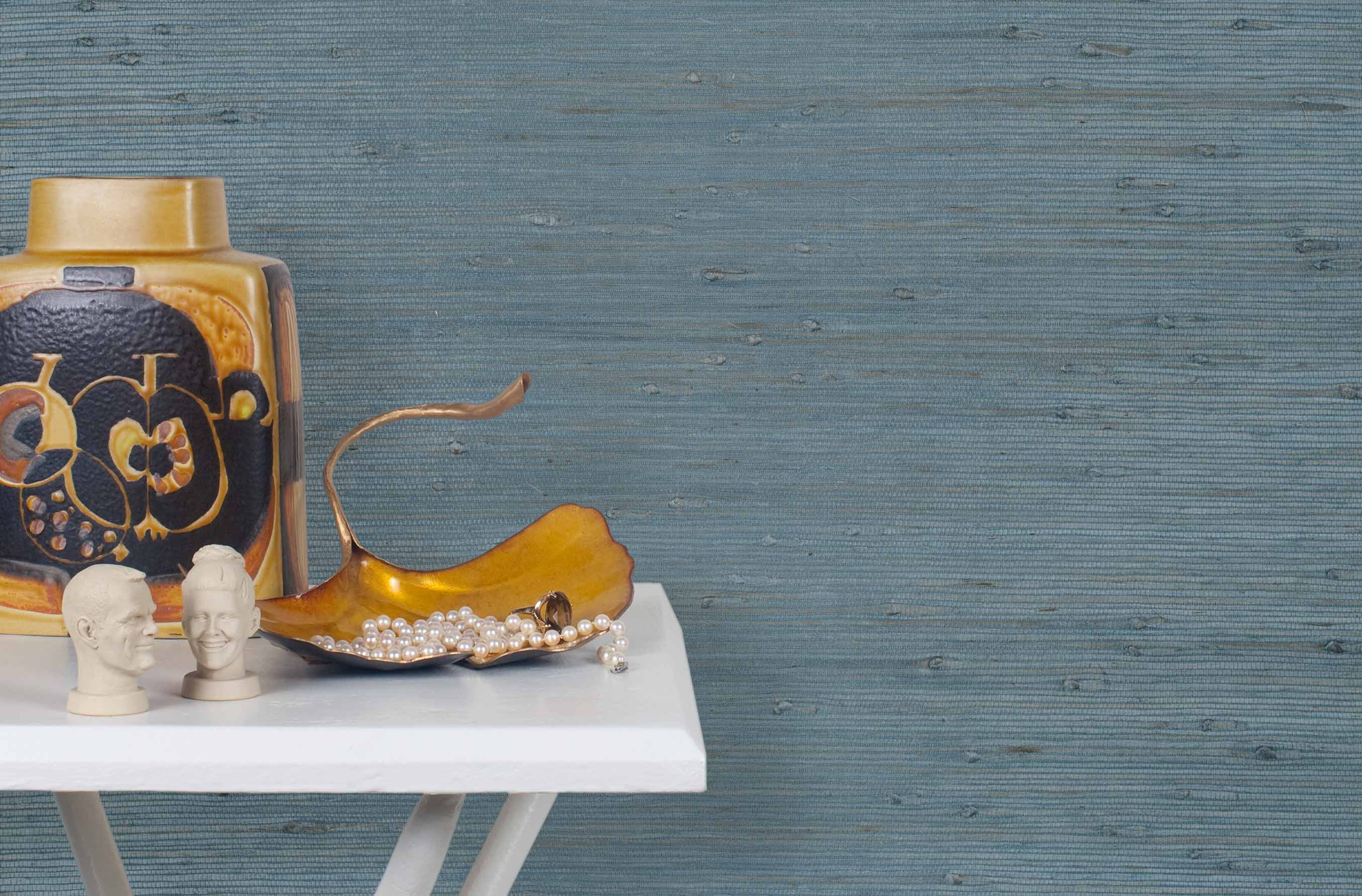 End table with a vase and sculptures in front of a wall papered in jute grasscloth in cadet blue.