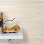 End table with a vase and sculptures in front of a wall papered in jute grasscloth in cream.