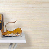 End table with a vase and sculptures in front of a wall papered in jute grasscloth in cream.
