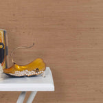 End table with a vase and sculptures in front of a wall papered in jute grasscloth in warm clay.