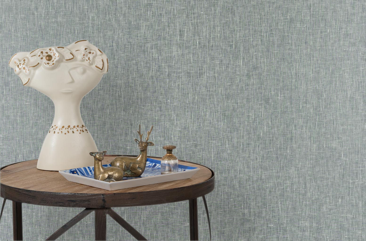 End table with a tray and some sculptures in front of a wall papered in textured grasscloth in steel blue.