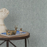 End table with a tray and some sculptures in front of a wall papered in textured grasscloth in steel blue.
