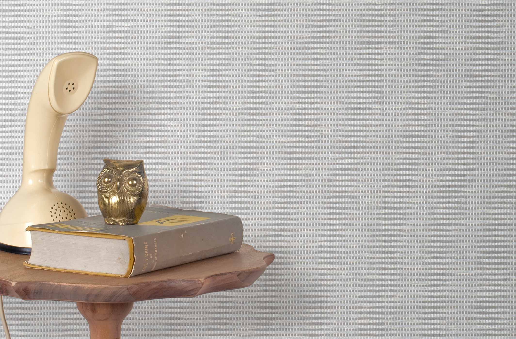 End table with a phone, book and owl sculpture in front of a wall covered in paperweave grasscloth in striped gray.
