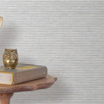 End table with a phone, book and owl sculpture in front of a wall covered in paperweave grasscloth in striped gray.