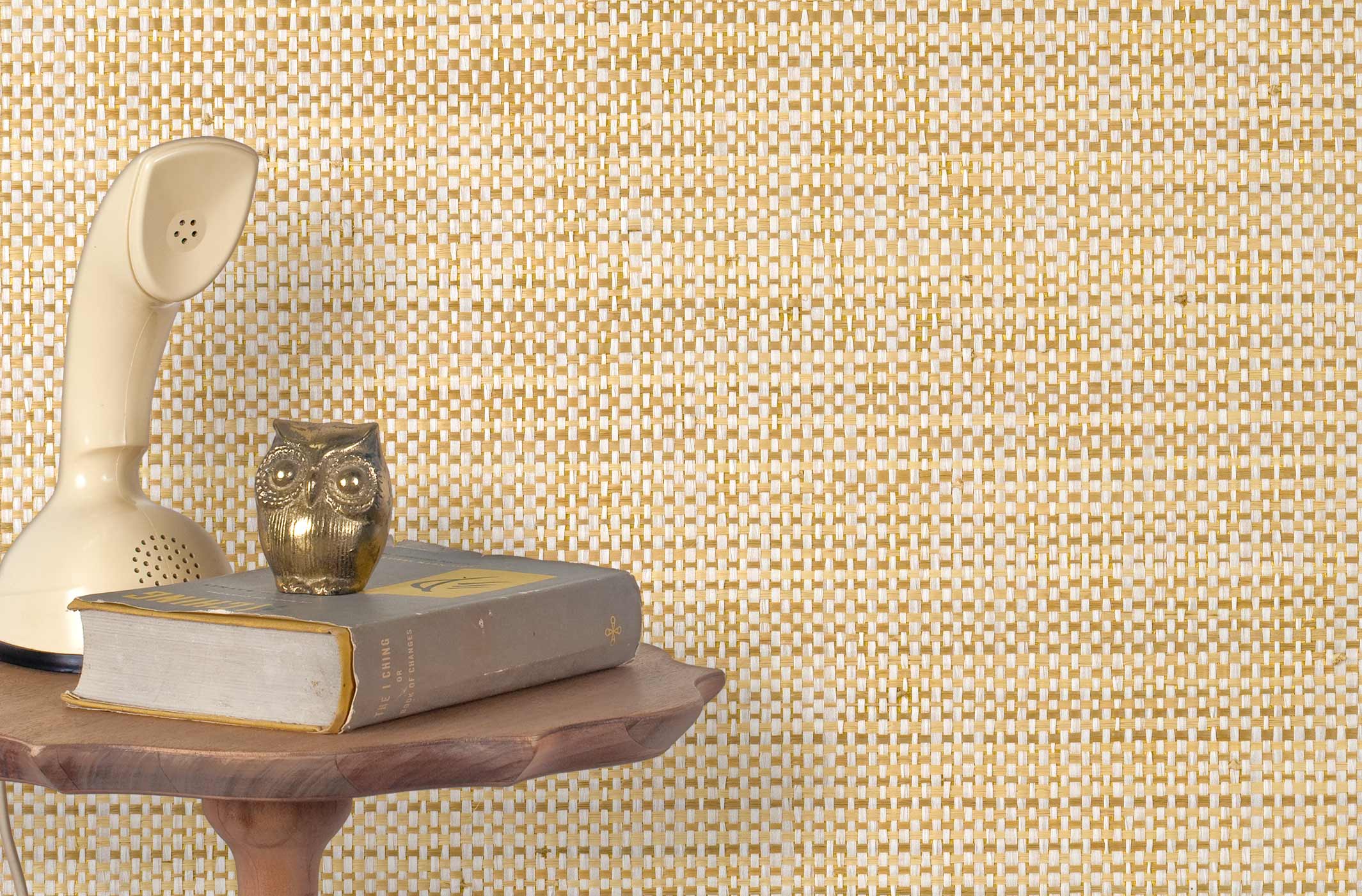 End table with a phone, book and owl sculpture in front of a wall covered in paperweave grasscloth in checked cream and tan.