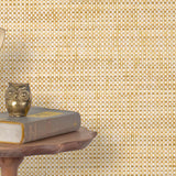 End table with a phone, book and owl sculpture in front of a wall covered in paperweave grasscloth in checked cream and tan.