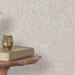 End table with a phone, book and owl sculpture in front of a wall covered in paperweave grasscloth in checked cream and gray.