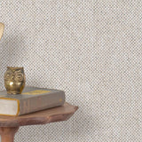 End table with a phone, book and owl sculpture in front of a wall covered in paperweave grasscloth in checked cream and gray.