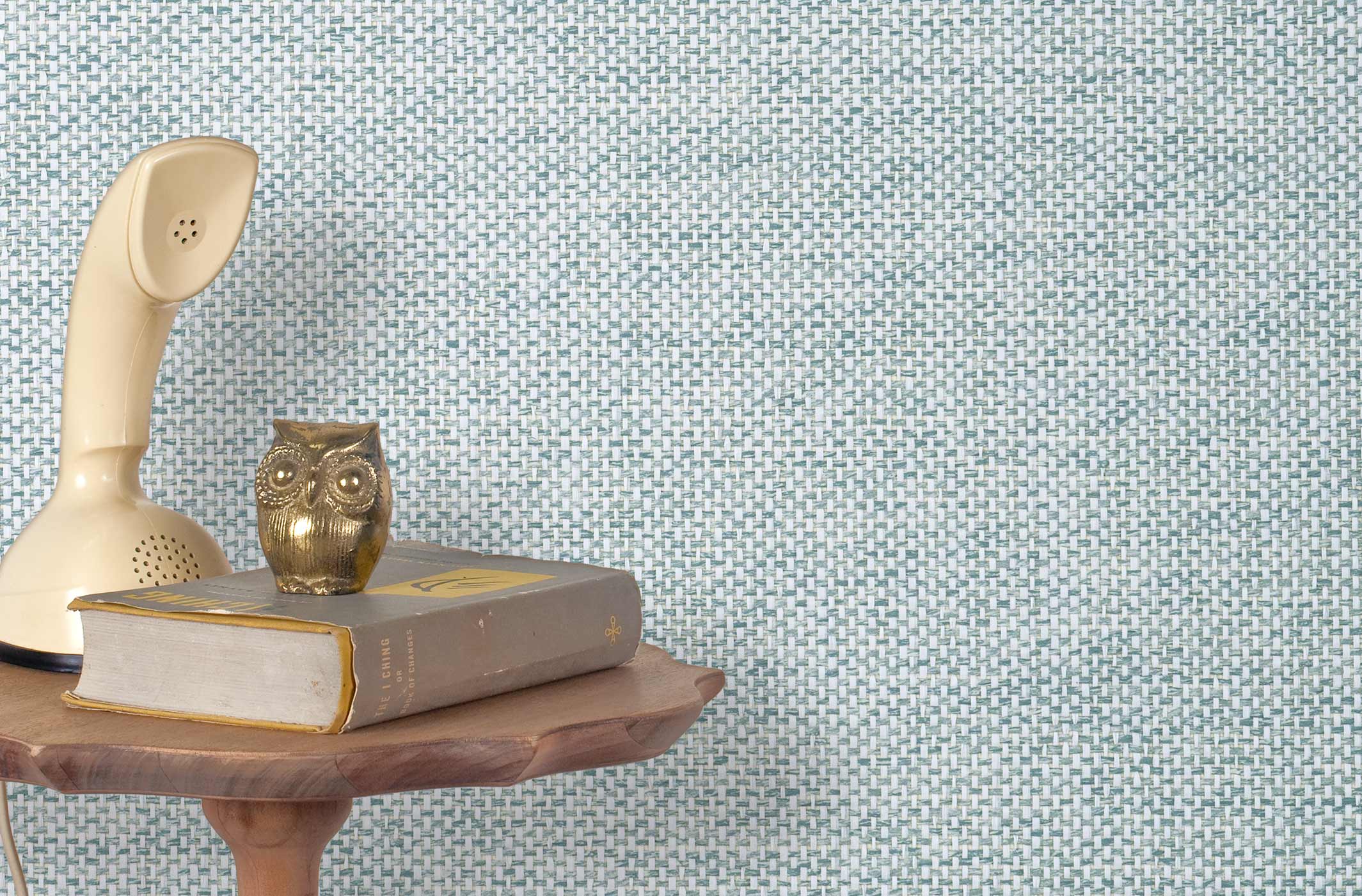 End table with a phone, book and owl sculpture in front of a wall covered in paperweave grasscloth in checked blue and white.