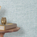 End table with a phone, book and owl sculpture in front of a wall covered in paperweave grasscloth in checked blue and white.