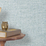 End table with a phone, book and owl sculpture in front of a wall covered in paperweave grasscloth in checked blue and white.