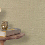 End table with a phone, book and owl sculpture in front of a wall covered in paperweave grasscloth in natural taupe.