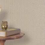 End table with a phone, book and owl sculpture in front of a wall covered in metallic paperweave grasscloth in tan.