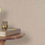 End table with a phone, book and owl sculpture in front of a wall covered in metallic paperweave grasscloth in tan.