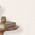 End table with a phone, book and owl sculpture in front of a wall covered in paperweave grasscloth in cream.