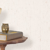 End table with a phone, book and owl sculpture in front of a wall covered in paperweave grasscloth in cream.