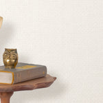 End table with a phone, book and owl sculpture in front of a wall covered in paperweave grasscloth in white.