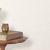 End table with a phone, book and owl sculpture in front of a wall covered in paperweave grasscloth in white.
