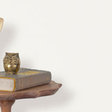 End table with a phone, book and owl sculpture in front of a wall covered in paperweave grasscloth in white.