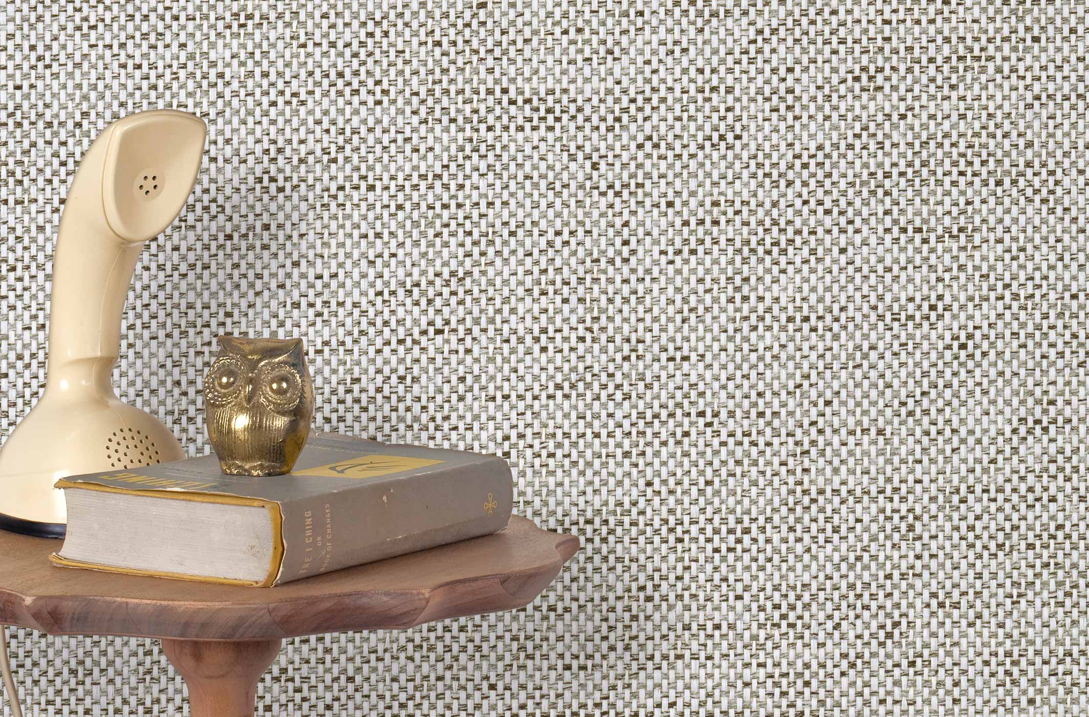 End table with a phone, book and owl sculpture in front of a wall covered in paperweave grasscloth in gray, black and white.