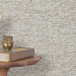 End table with a phone, book and owl sculpture in front of a wall covered in paperweave grasscloth in gray, black and white.