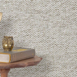 End table with a phone, book and owl sculpture in front of a wall covered in paperweave grasscloth in gray, black and white.
