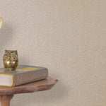 End table with a phone, book and owl sculpture in front of a wall covered in metallic paperweave grasscloth in neutral.