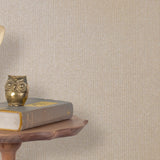 End table with a phone, book and owl sculpture in front of a wall covered in metallic paperweave grasscloth in neutral.
