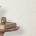 End table with a phone, book and owl sculpture in front of a wall covered in paperweave grasscloth in cream.