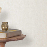 End table with a phone, book and owl sculpture in front of a wall covered in paperweave grasscloth in cream.