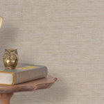 End table with a phone, book and owl sculpture in front of a wall covered in paperweave grasscloth in neutral.