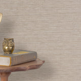 End table with a phone, book and owl sculpture in front of a wall covered in paperweave grasscloth in neutral.