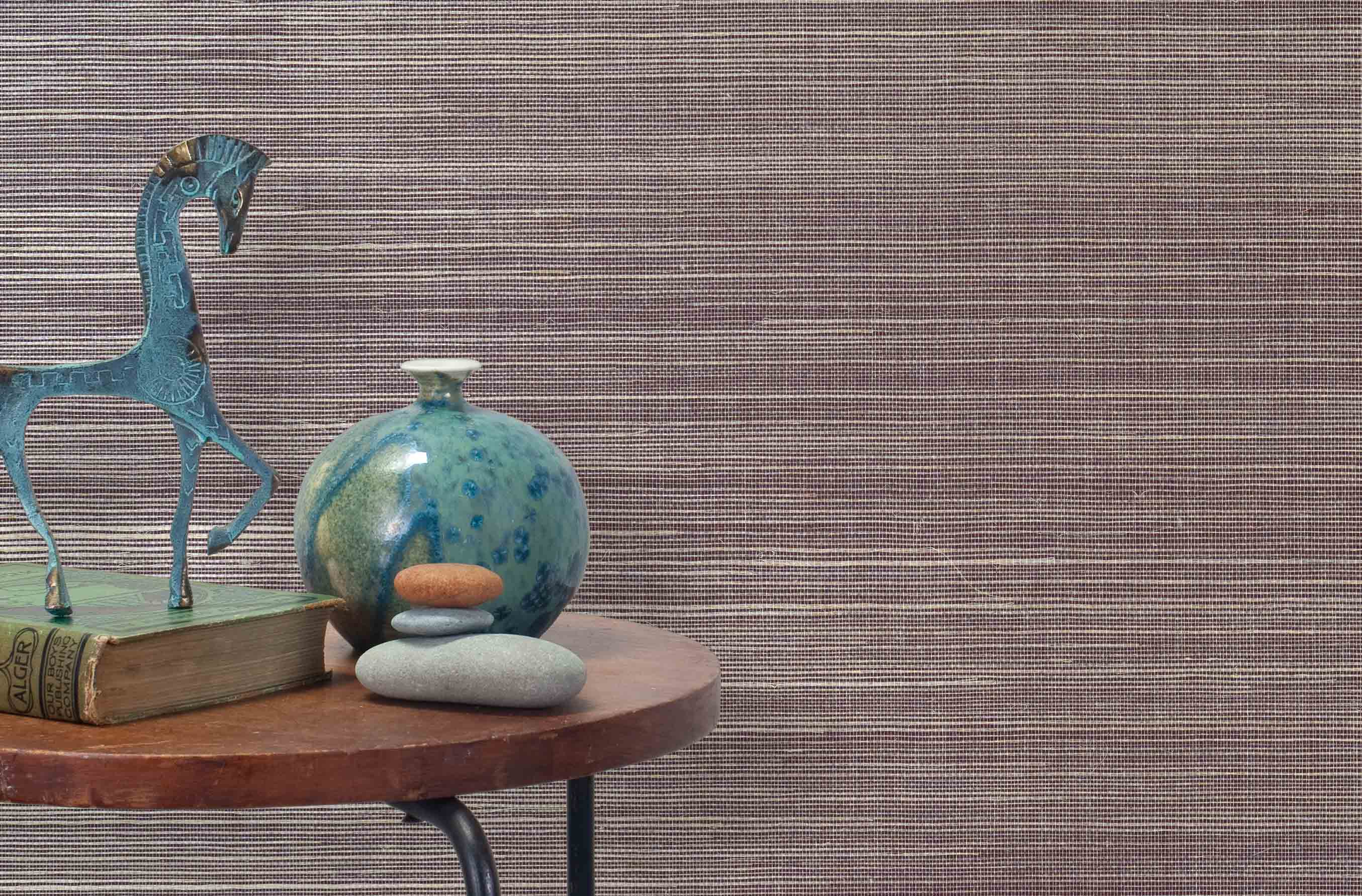 End table with a vase, horse sculpture and stones in front of a wall covered in sisal grasscloth in cream and maroon.