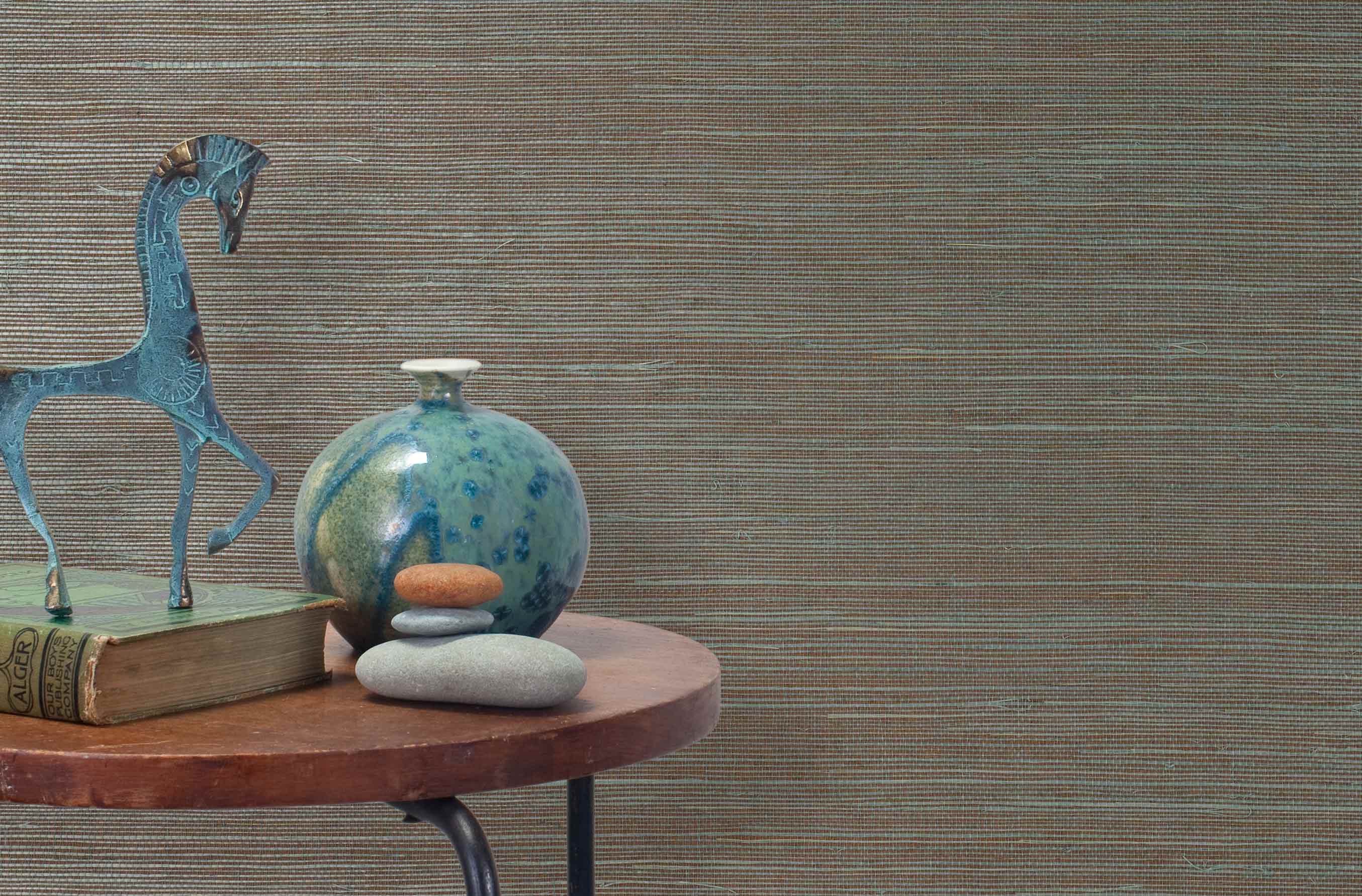 End table with a vase, horse sculpture and stones in front of a wall covered in sisal grasscloth in blue and brown.