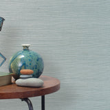 End table with a vase, horse sculpture and stones in front of a wall covered in sisal grasscloth in pastel blue and white.