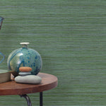 End table with a vase, horse sculpture and stones in front of a wall covered in sisal grasscloth in mottled green.