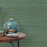 End table with a vase, horse sculpture and stones in front of a wall covered in sisal grasscloth in mottled green.